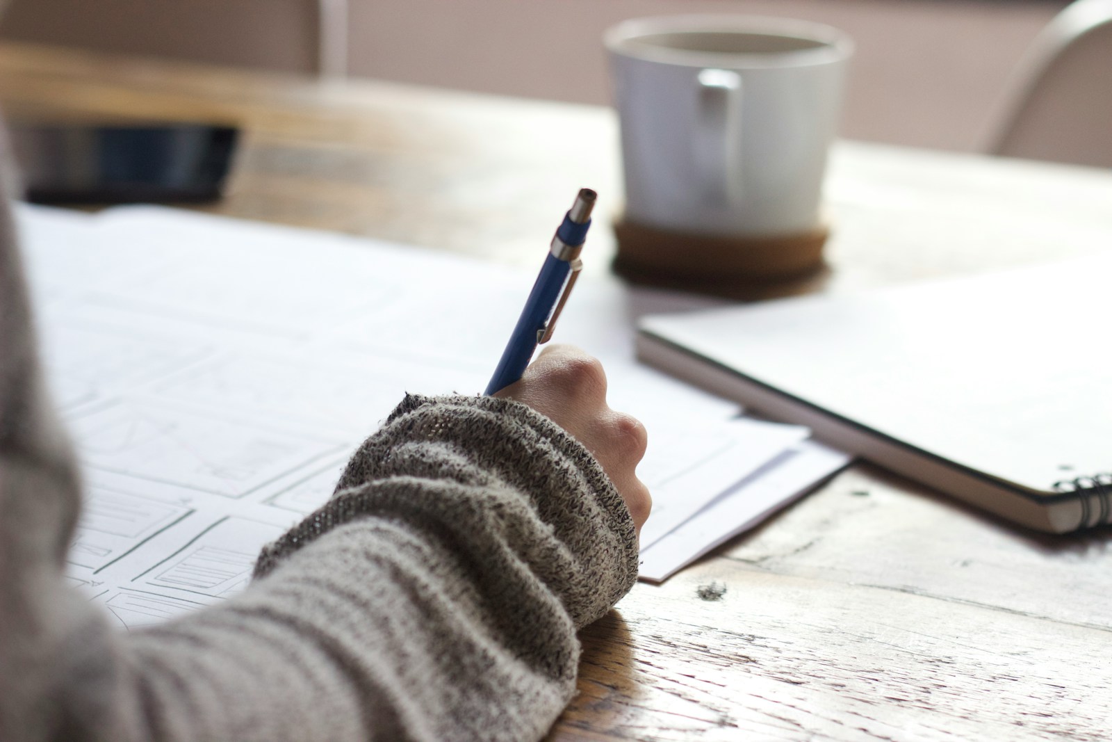 person writing on brown wooden table near white ceramic mug completing general liability insurance documents