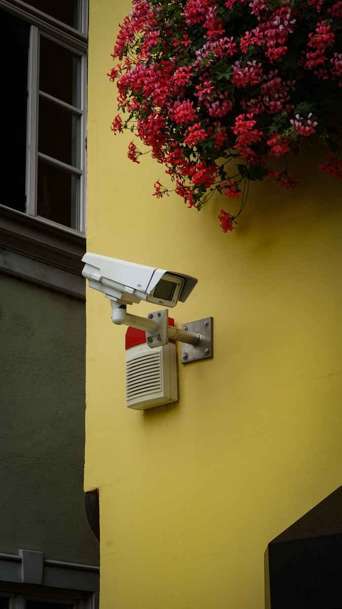 white and gray home security system camera mounted on yellow painted wall